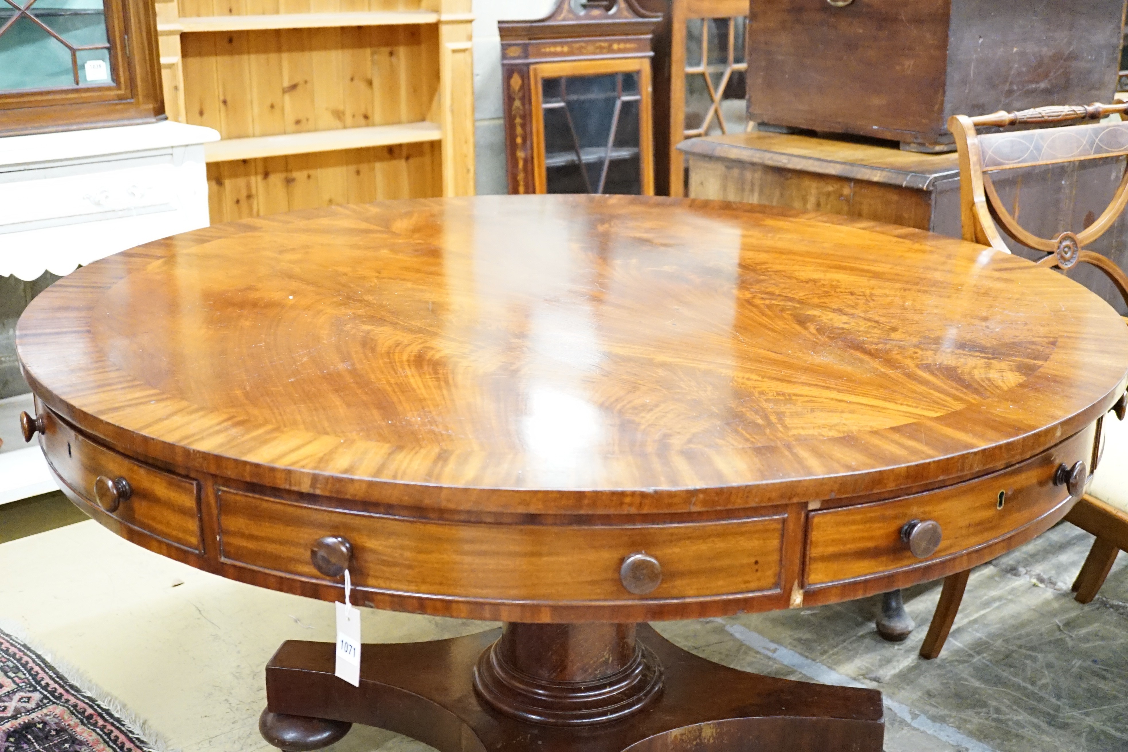 An early Victorian flame mahogany drum top ‘rent’ table, fitted four drawers on turned column saltire platform and brass castors, diameter 138cm, height 74cm